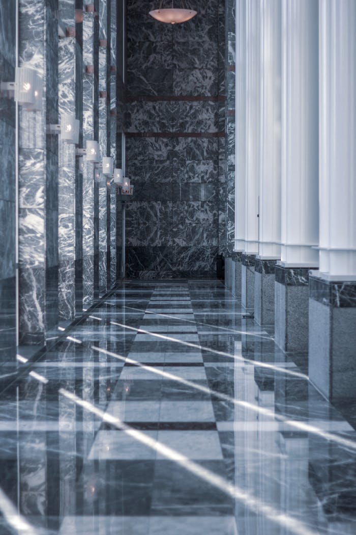 who-we-are Modern marble hallway with tall columns and reflective surfaces illuminated by daylight.